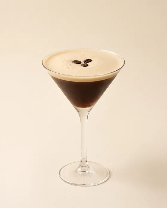 Espresso Martini — a coupe with a coffee-brown cocktail topped with crema foam and three beans, on a cream background